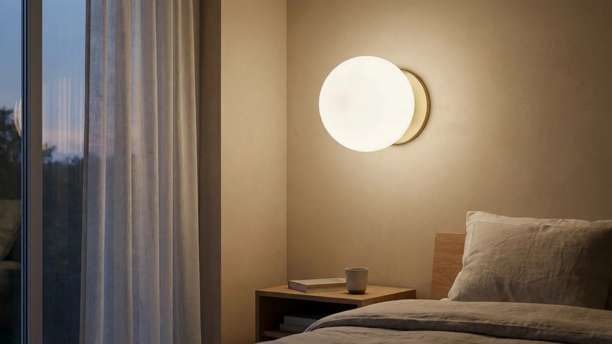 Applique murale boule en verre opalin allumée comme une lune douce sur un mur beige