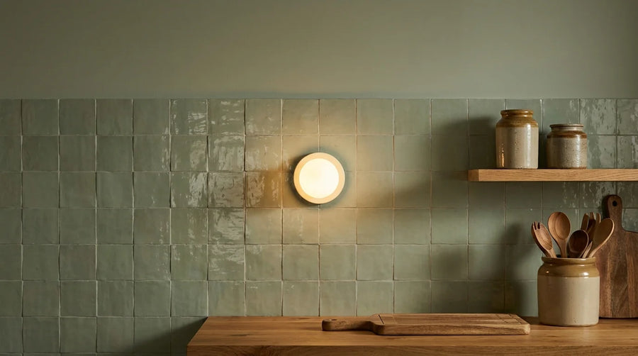 Mini applique murale à globe opale allumée au-dessus d'un plan de travail dans une cuisine vert sauge