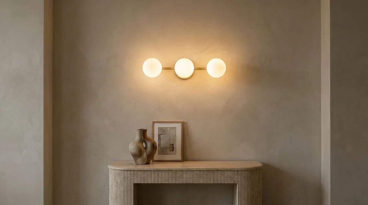 Applique murale dorée à trois globes allumée au-dessus d'une console en travertin