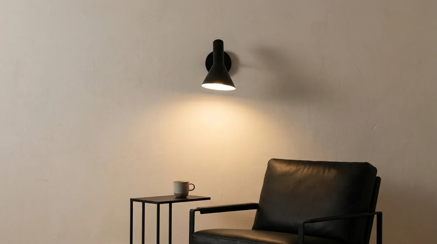 Applique murale noire à cône asymétrique allumée au-dessus d'un fauteuil en cuir