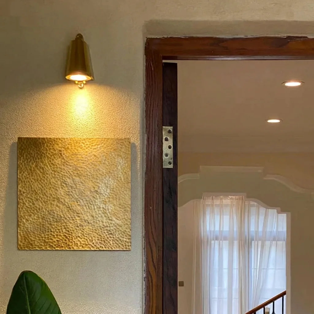 Applique cloche cuivrée éclairant une plaque en laiton martelé près d'une porte