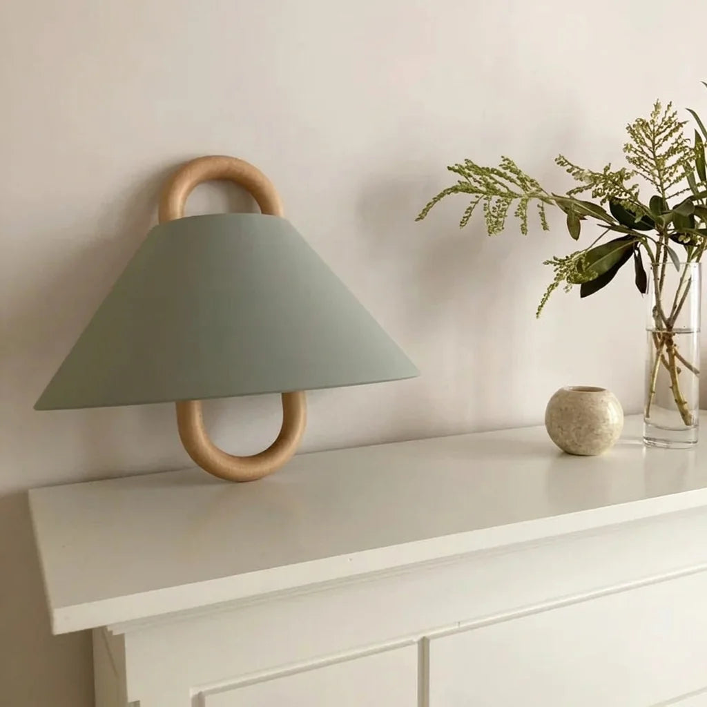 Applique abat-jour vert sauge au-dessus d'une commode avec un bouquet