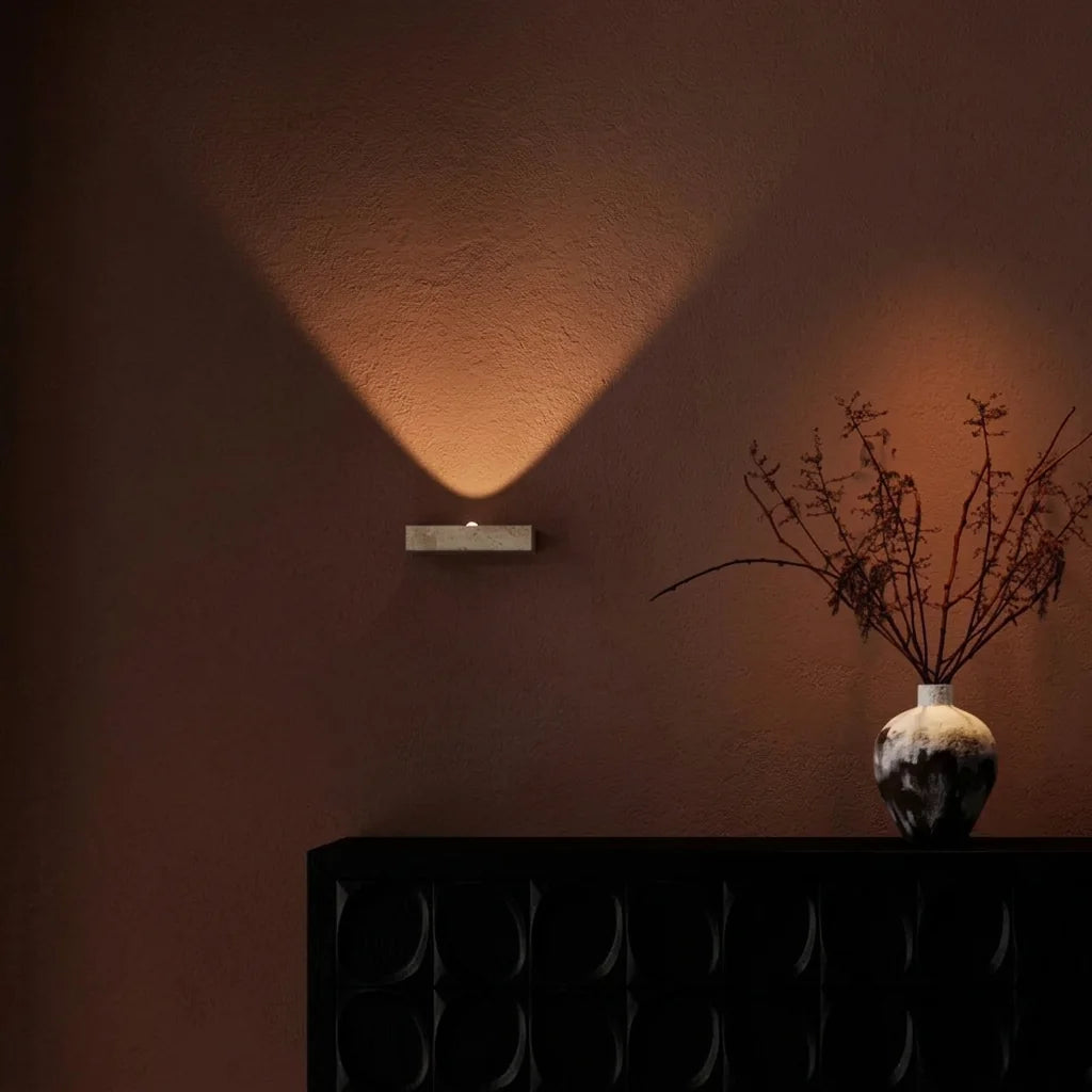 Applique en travertin projetant un faisceau sur un mur terracotta au-dessus d'un buffet noir