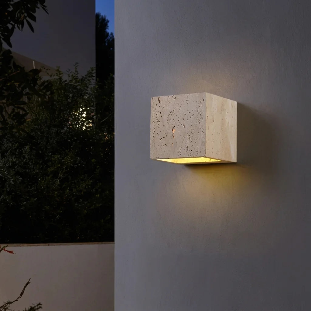 Applique cube en travertin sur une façade grise, la nuit