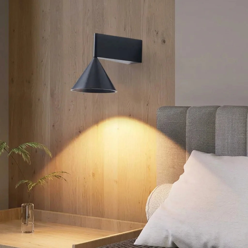 Applique cône noire éclairant une table de chevet sur un mur en bois