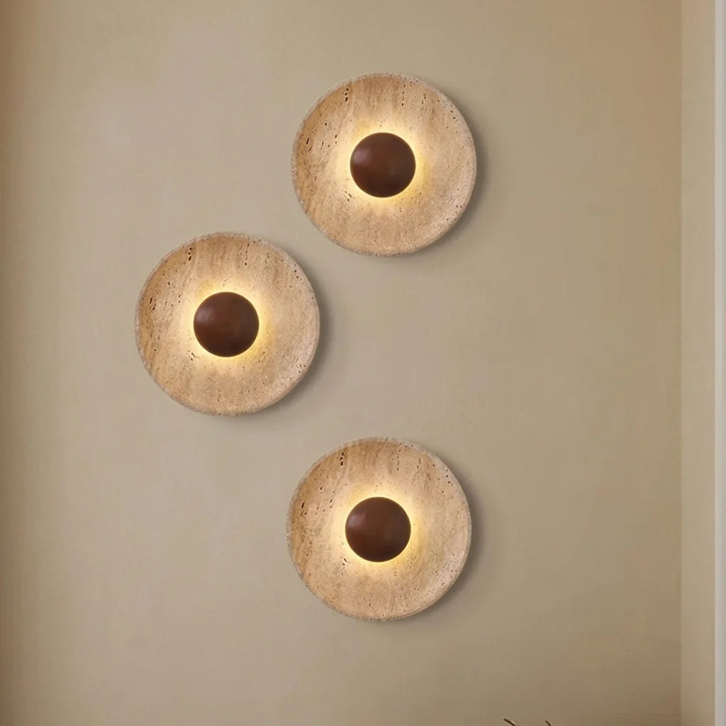 Composition de trois appliques disque en travertin sur un mur beige