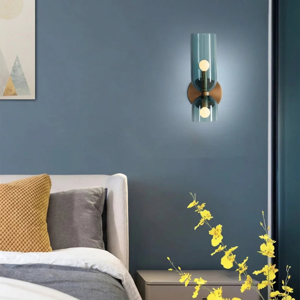 Applique en verre bleu allumée sur un mur bleu au-dessus d'un lit