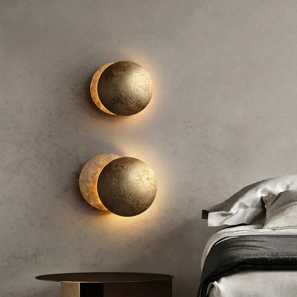 Deux appliques éclipse dorées sur un mur en béton à côté d'un lit