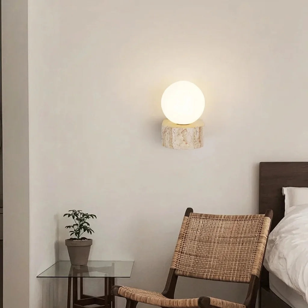 Applique globe sur travertin près d'un lit et d'un fauteuil en rotin