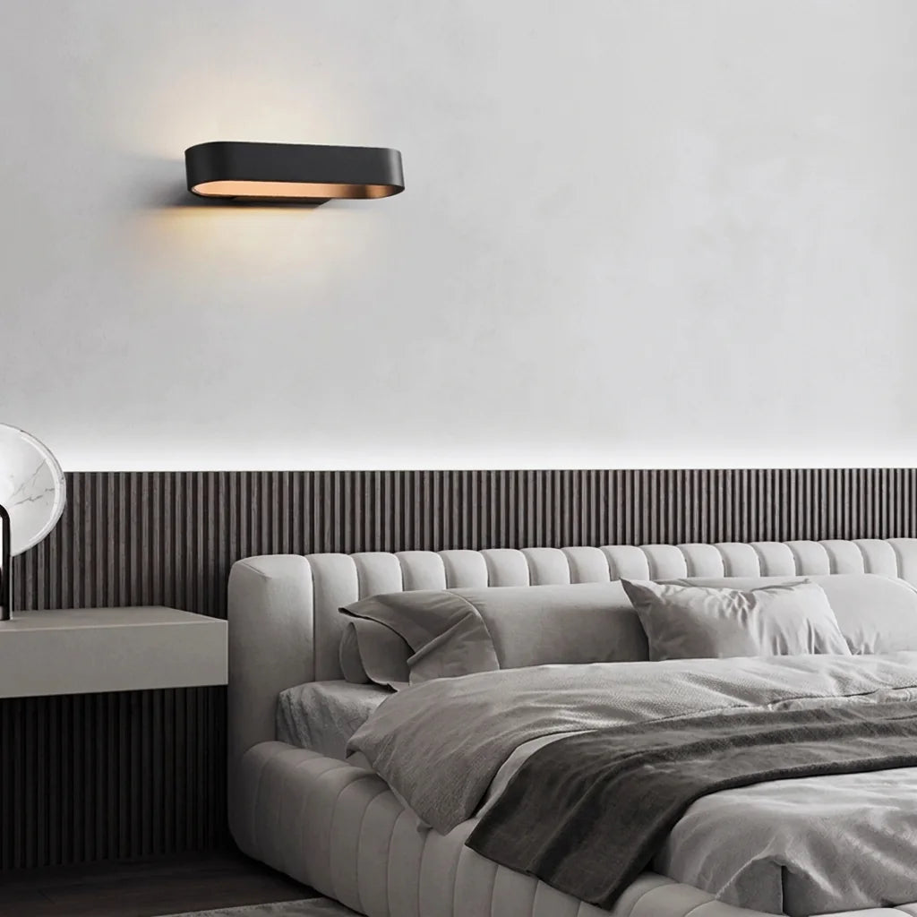 Applique LED ovale noire au-dessus d'un lit capitonné gris