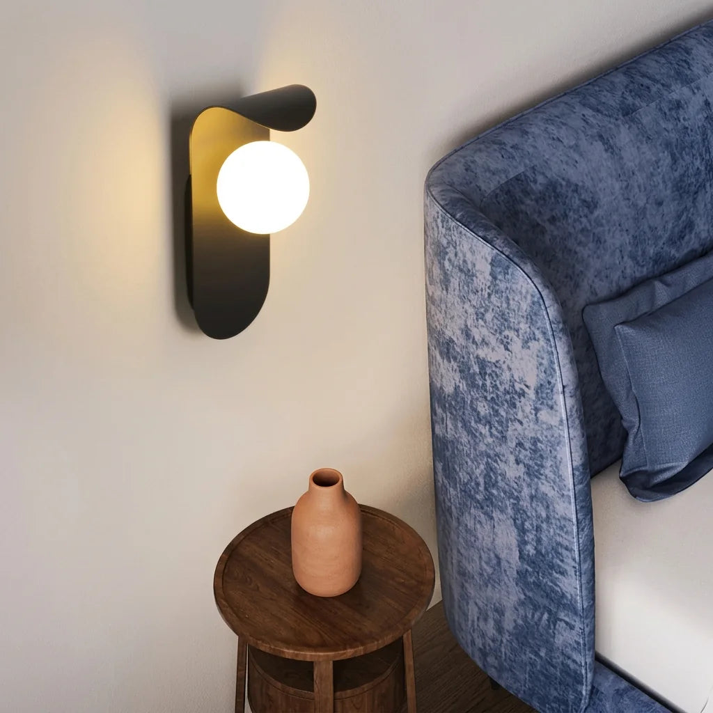 Applique LED noire à globe au-dessus d'un guéridon en bois, près d'un lit en velours bleu