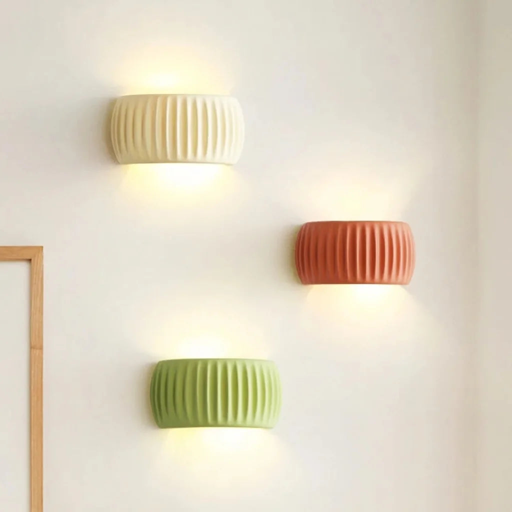Trois appliques cannelées crème, terracotta et vert sur un mur blanc