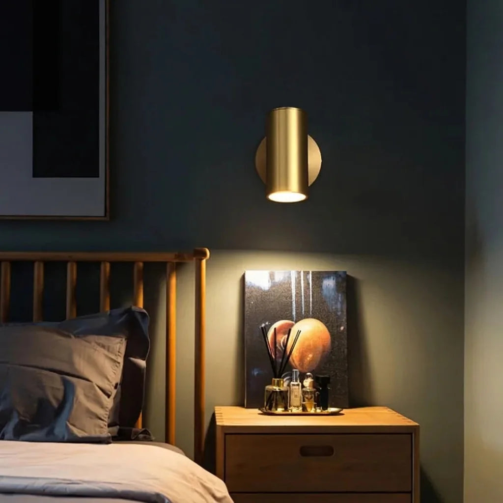 Spot cylindre doré au-dessus d'une table de chevet en bois, mur bleu nuit