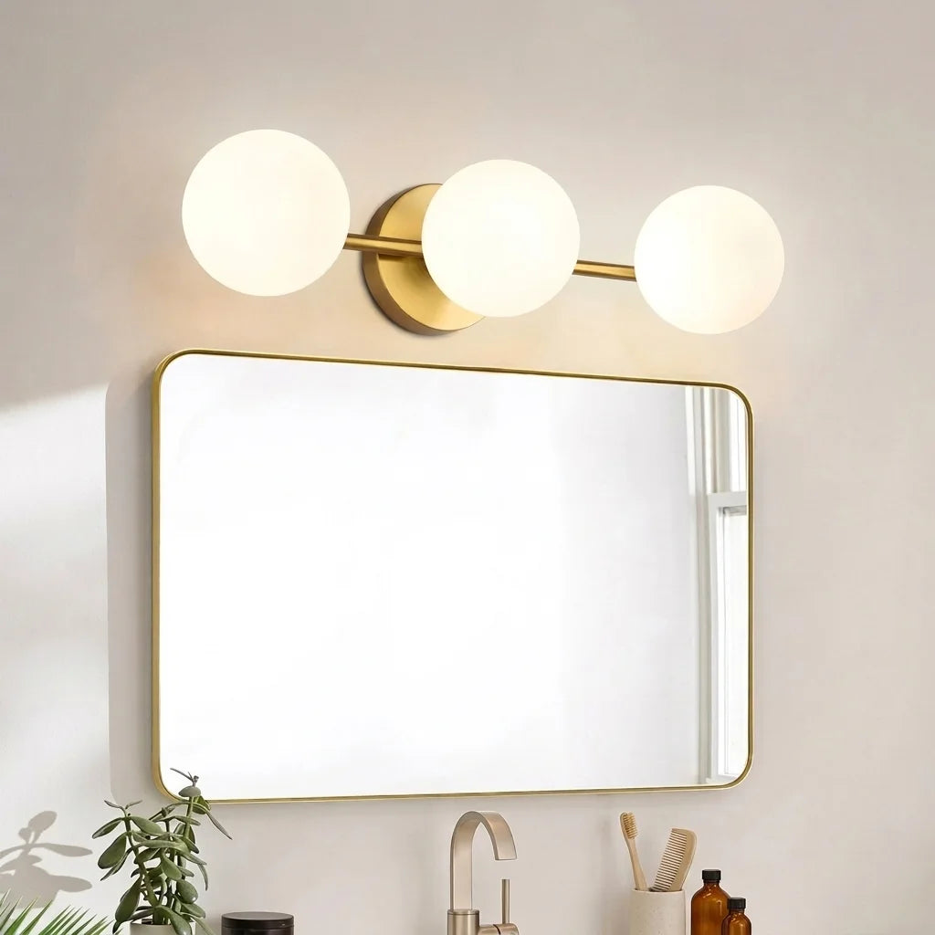Applique trois globes dorée au-dessus d'un miroir de salle de bain