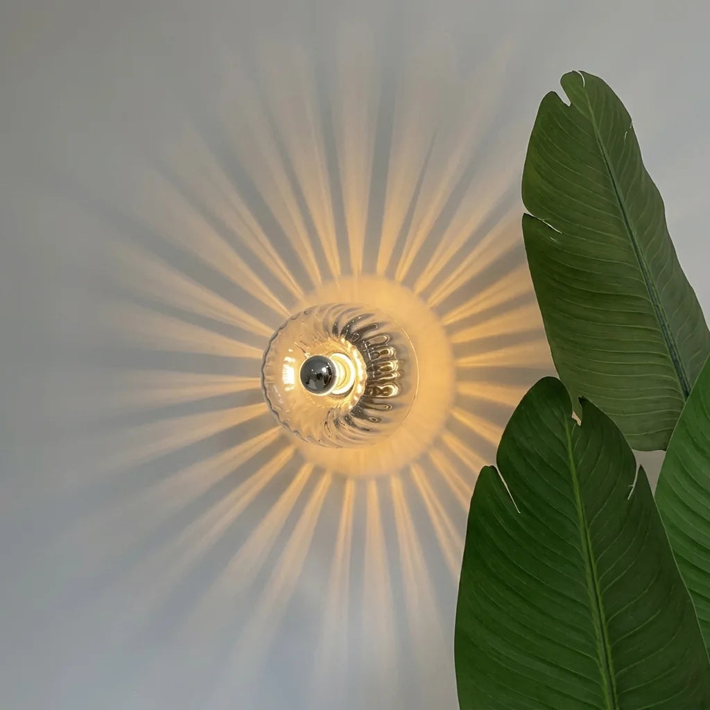 Applique en verre cannelé projetant un soleil lumineux près de feuilles de bananier