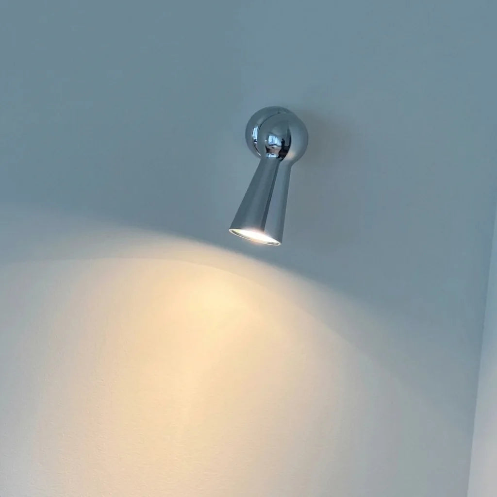 Spot conique chromé éclairant un mur bleu-gris