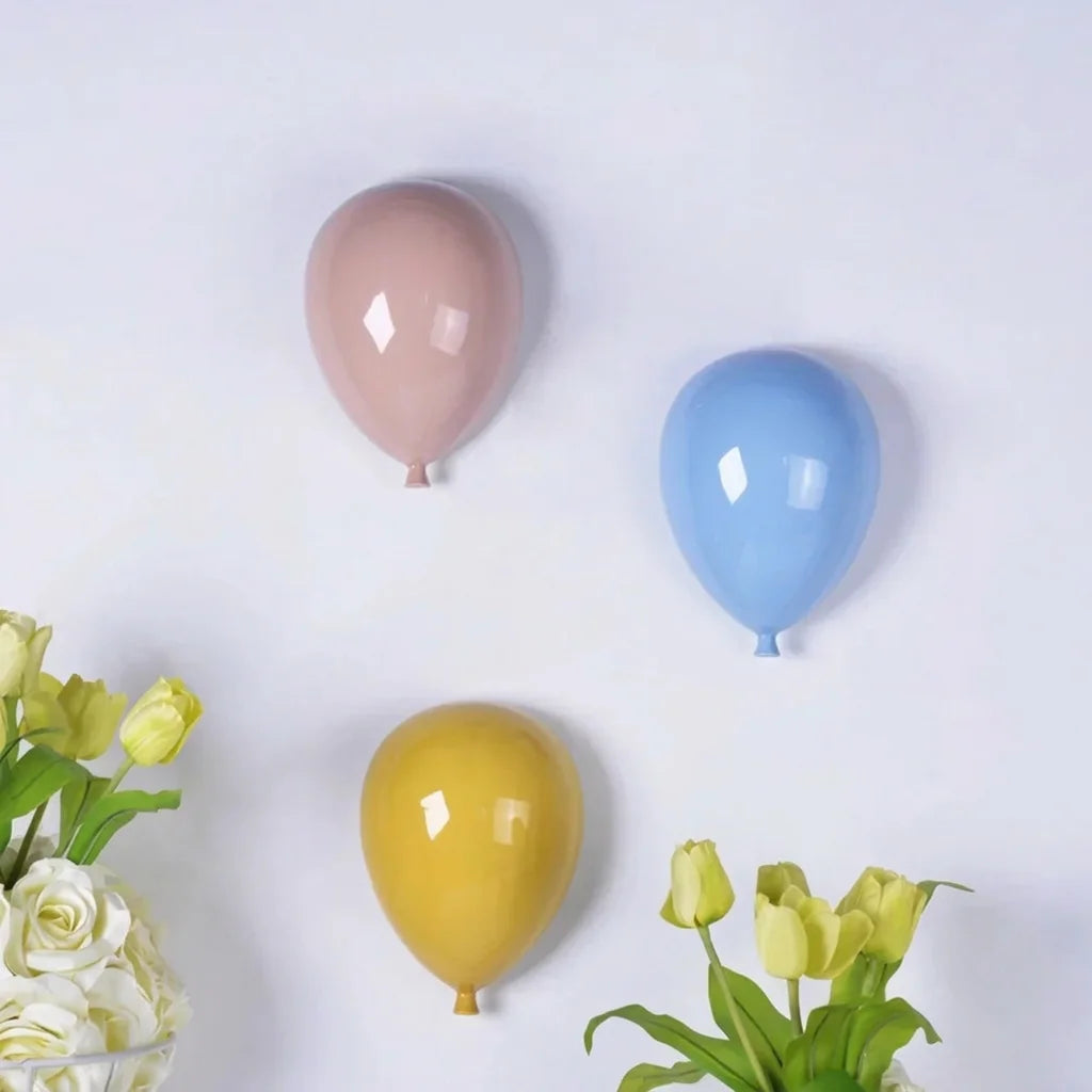 Ballons en céramique rose, bleu et jaune sur un mur clair fleuri